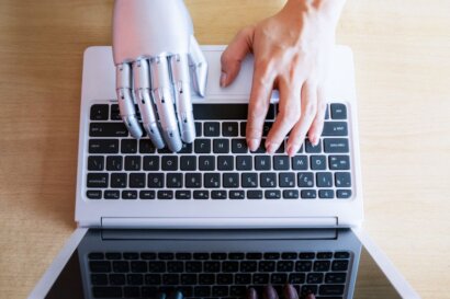 a left human and right robot hands typing on a laptop keyboard represents AI and Human