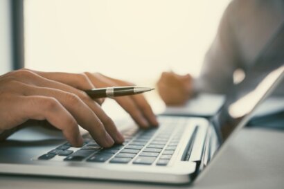 a hand holding a pen while typing on a laptop computer