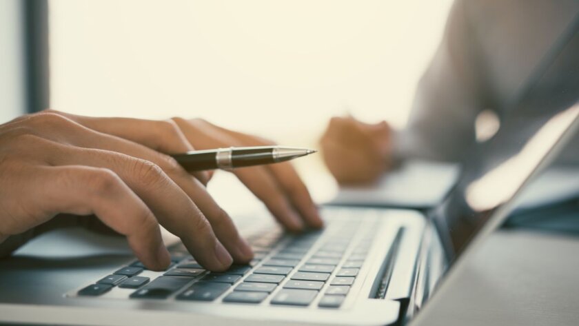 a hand holding a pen while typing on a laptop computer